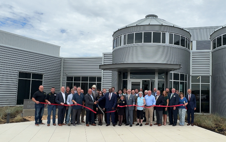 A group of individuals gathered in front of a building, preparing to cut a ribbon for an opening ceremony.
